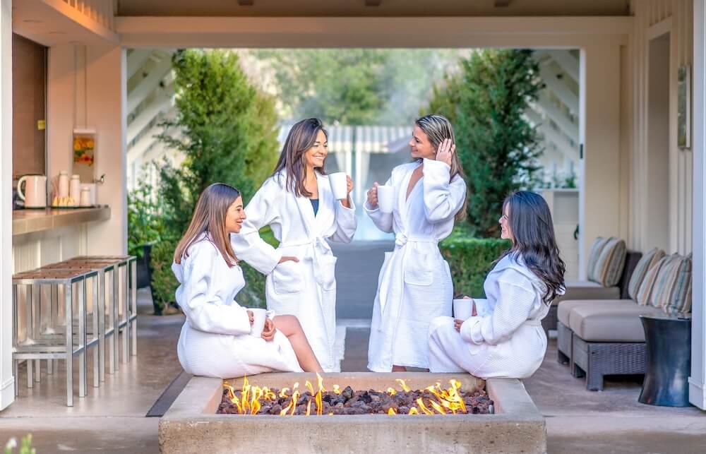 women sitting around fire pit at spa wearing bath robes
