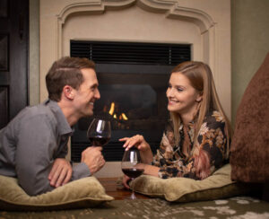 couple laying on carpet by fireplace drinking wine