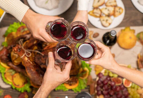 wine glasses held over table of food