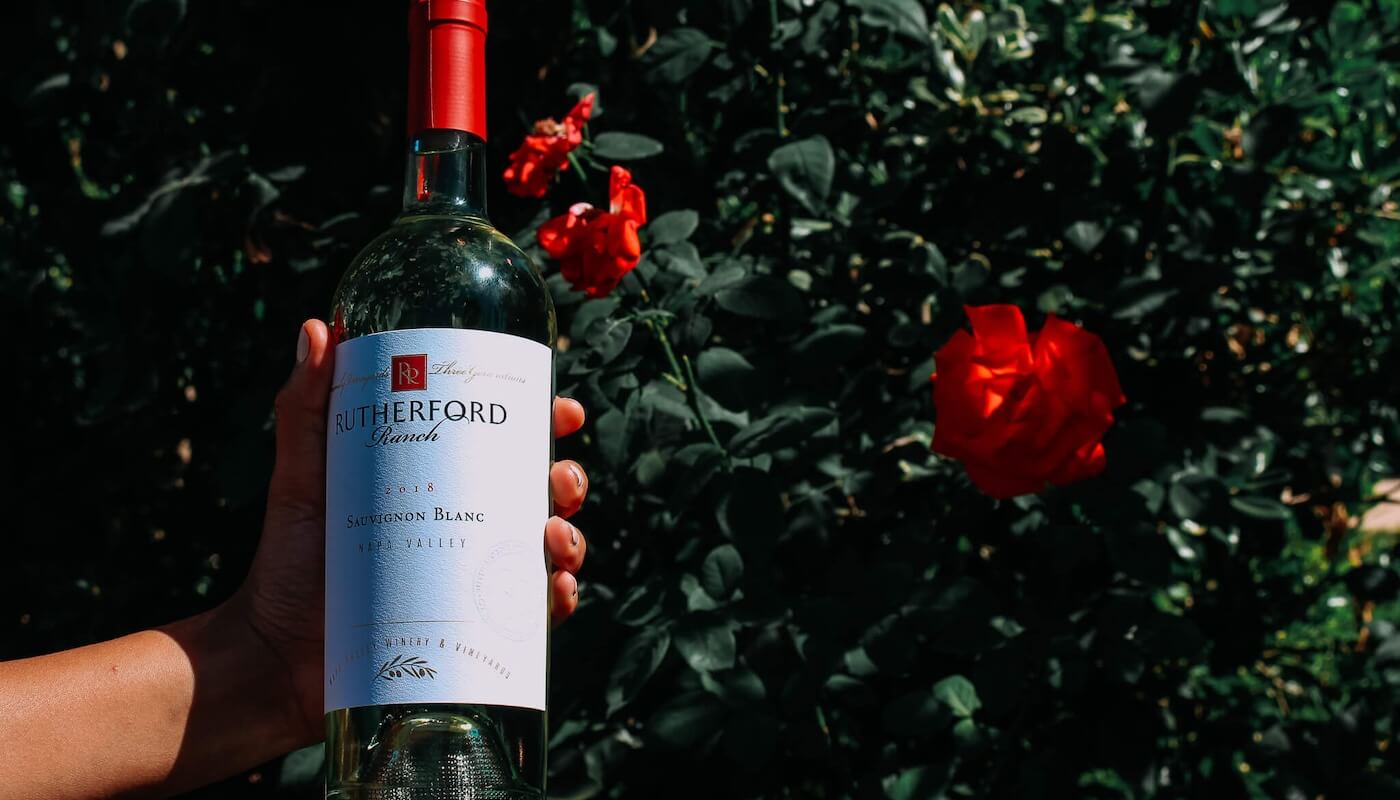 hand holding wine bottle in rose bush