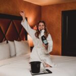 woman wearing bath robe opening champagne in hotel room