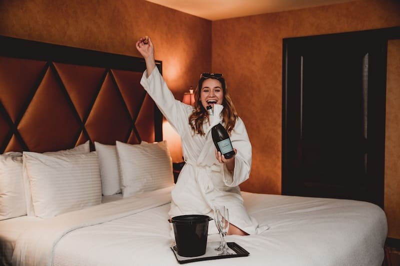 woman wearing bath robe opening champagne in hotel room