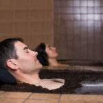 man and woman relaxing on separate mud baths