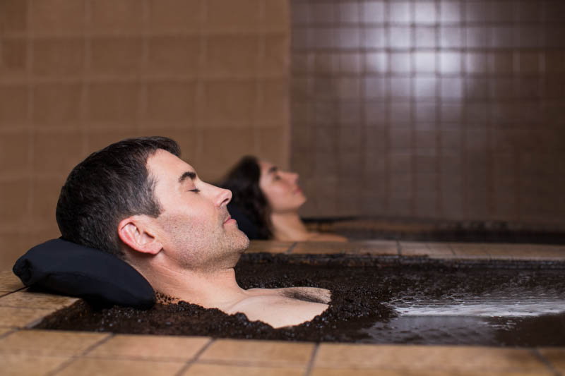 man and woman relaxing on separate mud baths
